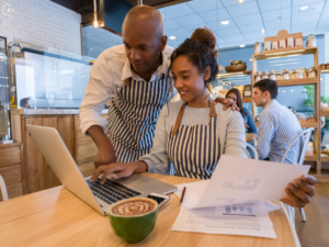 Man and woman looking at papers and laptop in restaurant