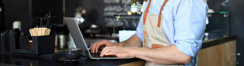 Restaurant manager wearing an apron working on laptop at cafe bar.